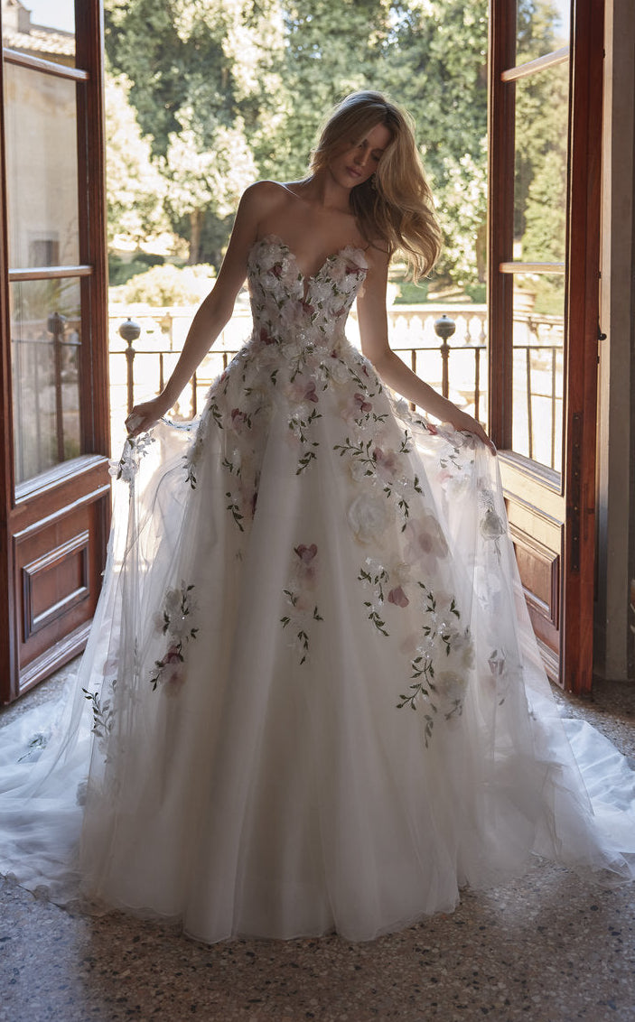 Woman in a floral wedding dress standing in a room with large windows.