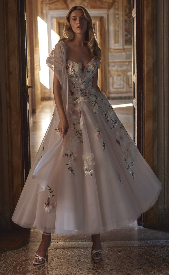 Woman in a floral dress standing in an ornate room with sunlight streaming in.