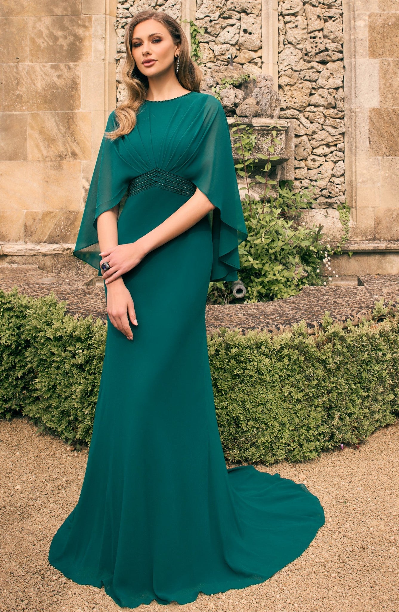Woman in a green evening gown standing in front of a stone building with a decorative arch.