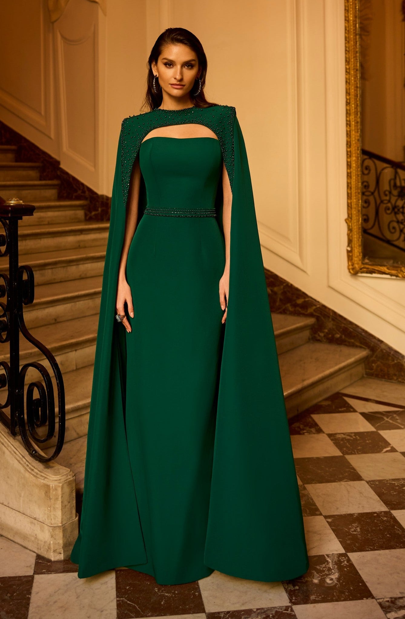 Woman in a green dress with cape standing in an elegant interior setting