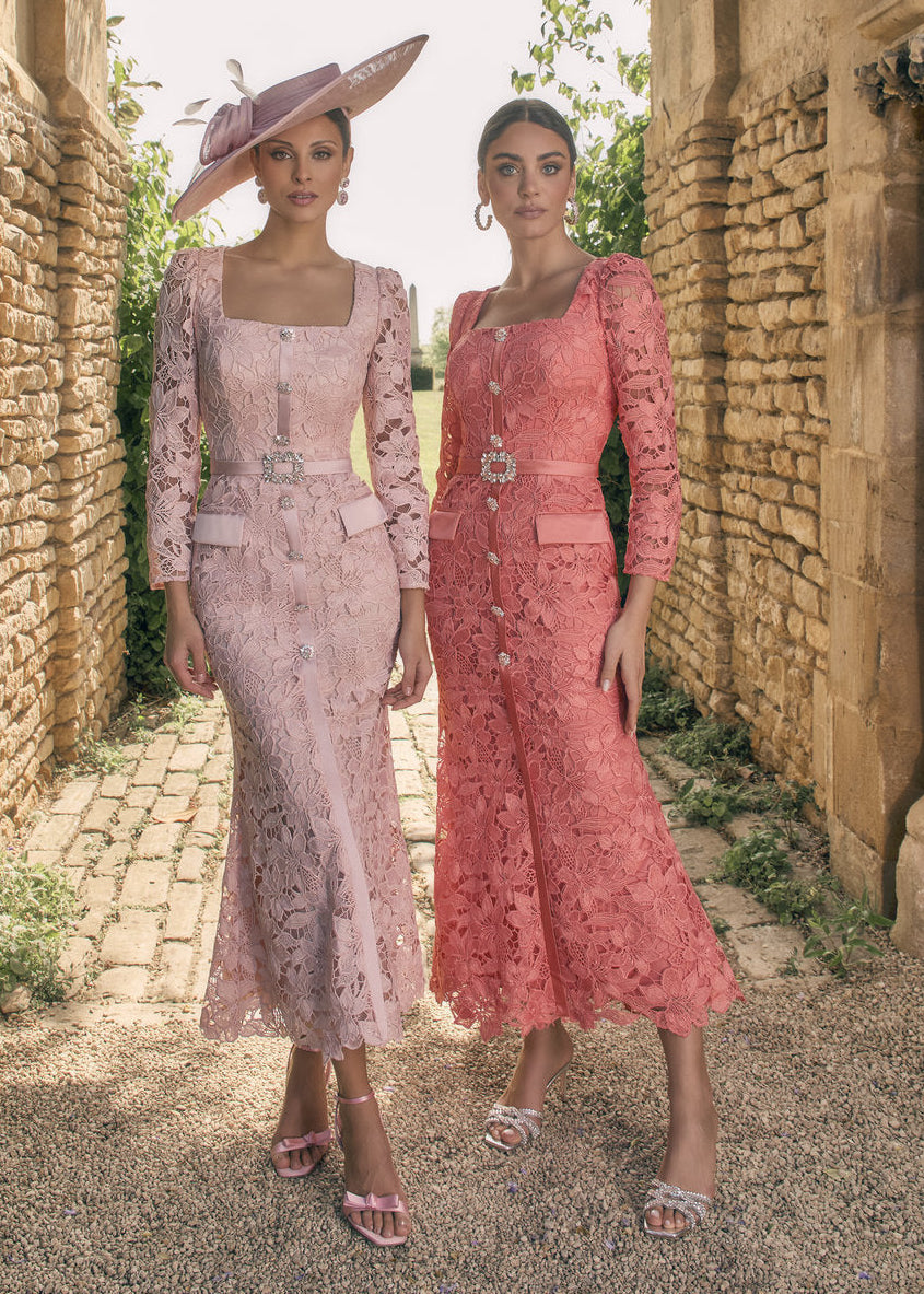 Two women in elegant dresses standing in a stone archway with a chandelier above.