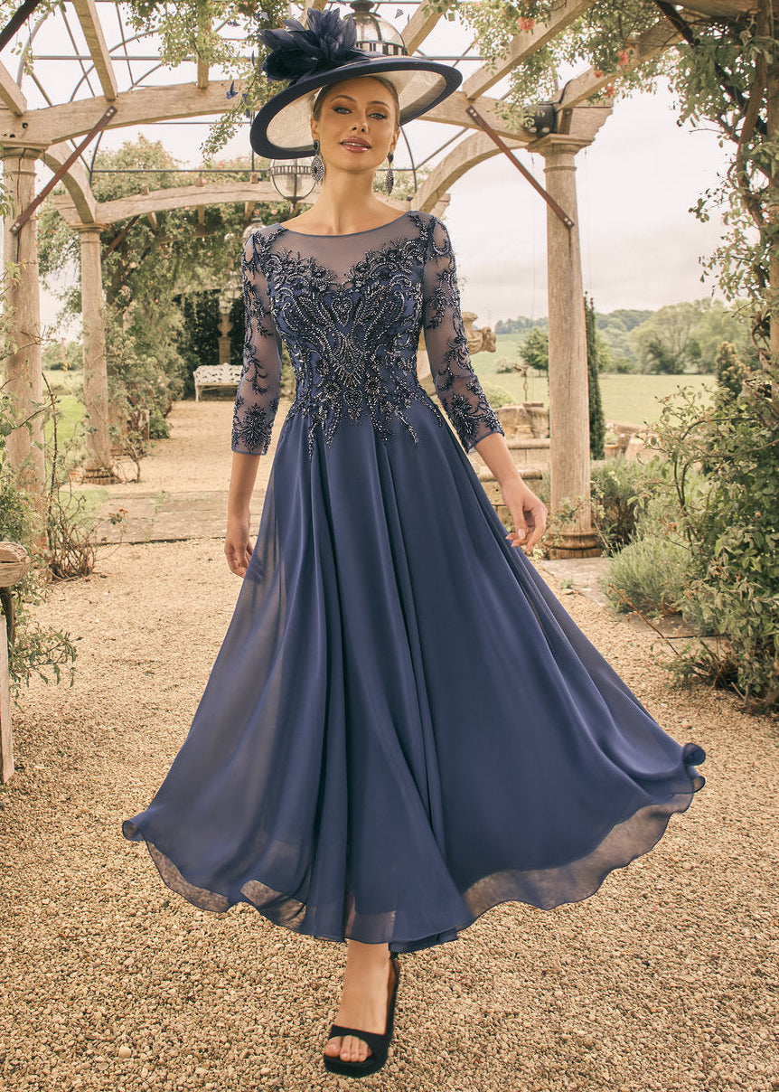 Woman in a blue dress with lace detailing standing under a wooden arbor in a garden.