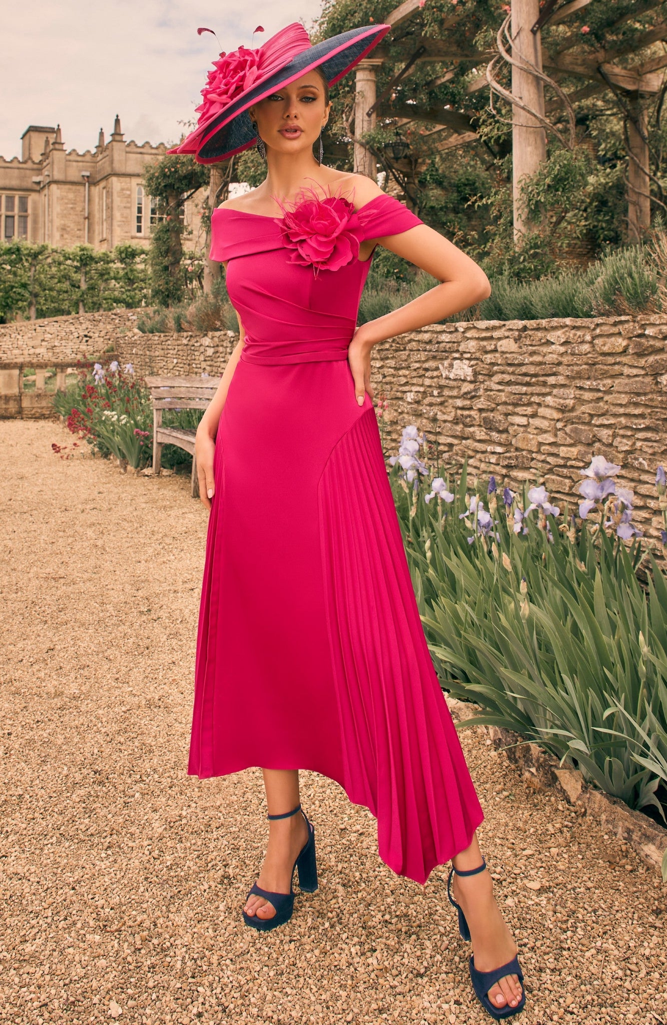 Woman in a pink dress with a floral hat standing in a garden setting.