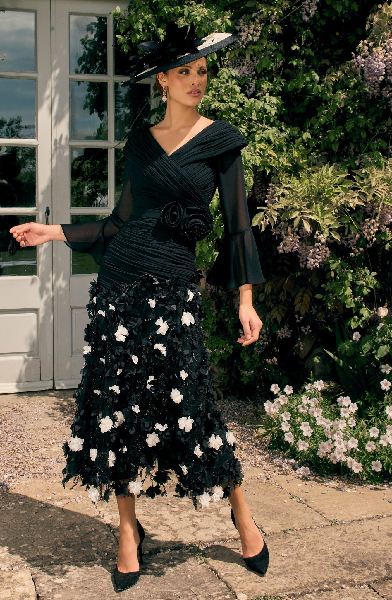 Woman in a black dress with floral details standing in a garden.