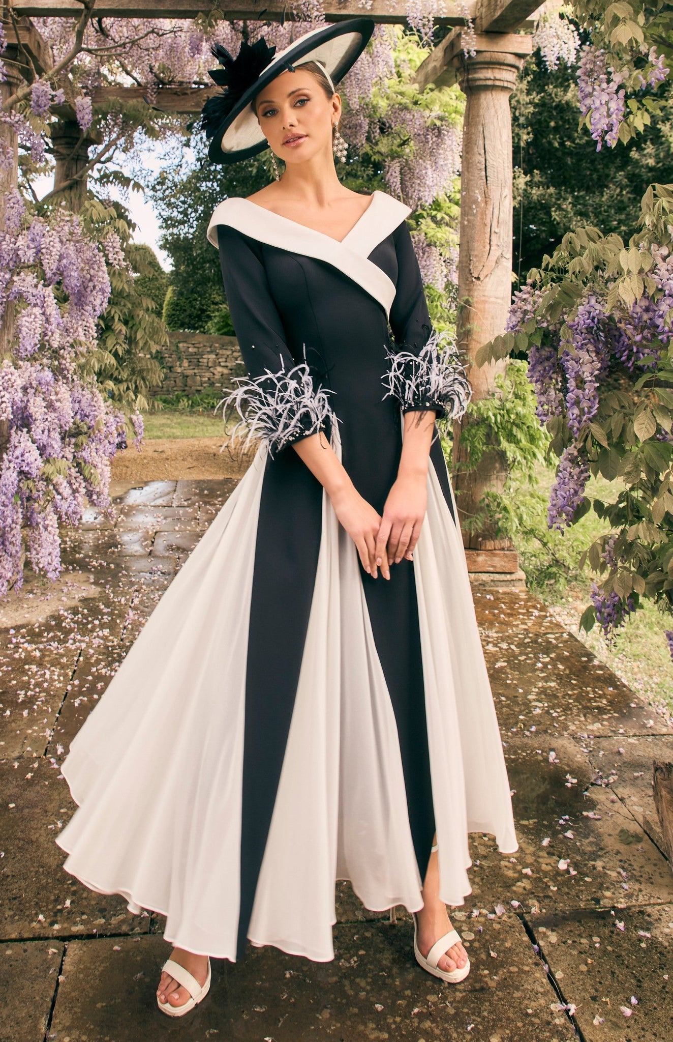 Woman in a black and white dress standing under a wisteria archway.