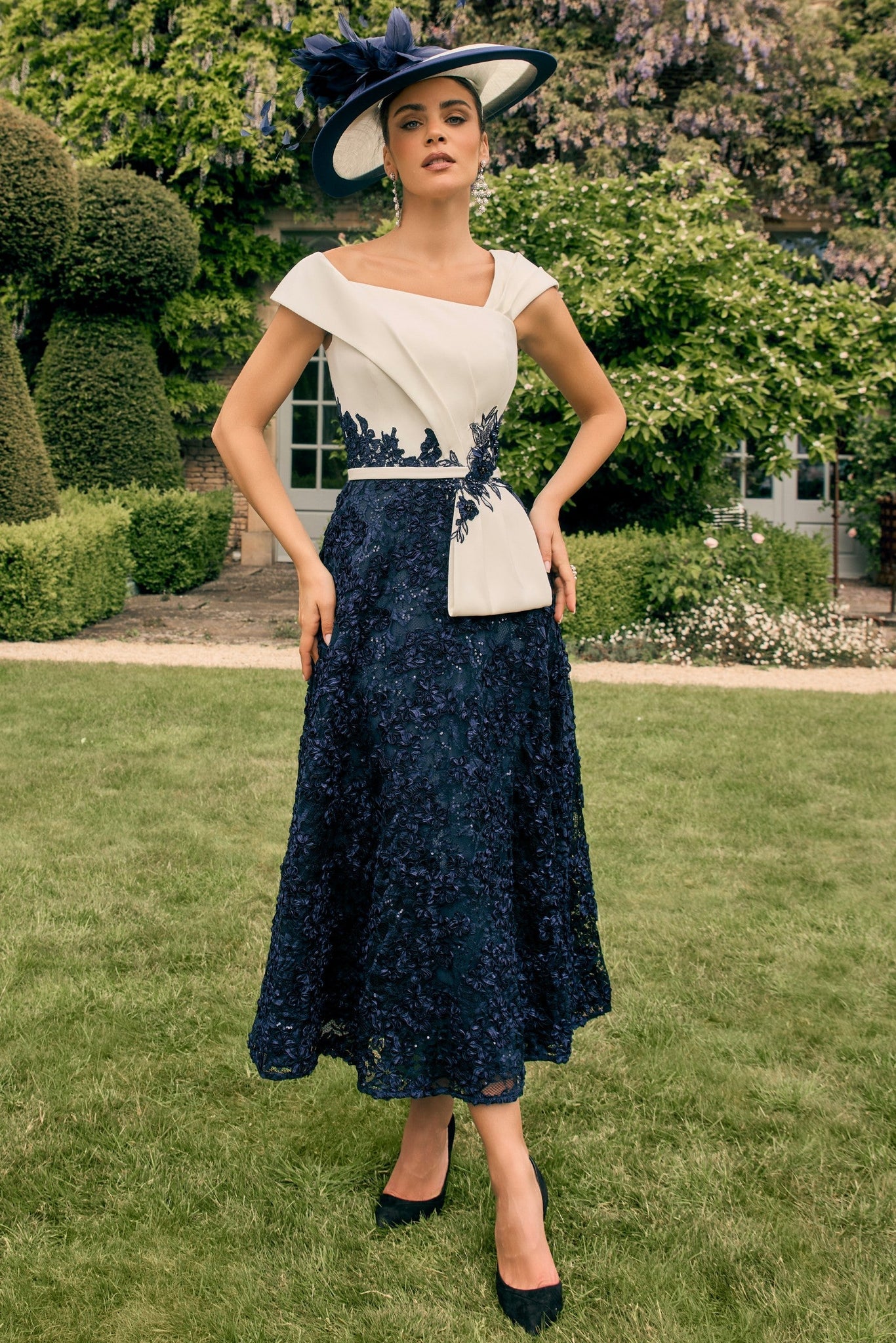 Woman in a navy and white dress with a matching hat standing in a garden.