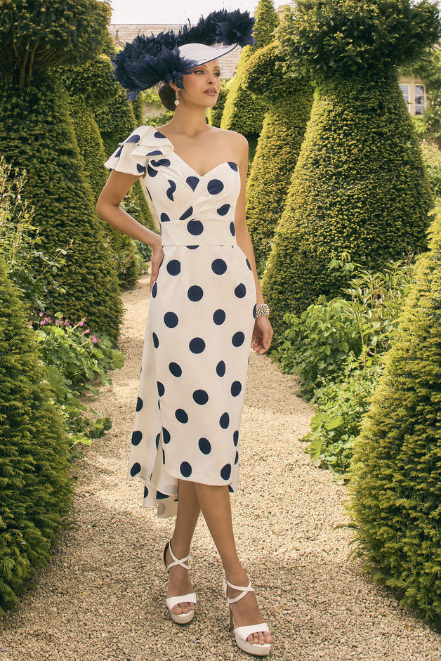 Woman in a polka dot dress and hat walking through a garden with topiary.