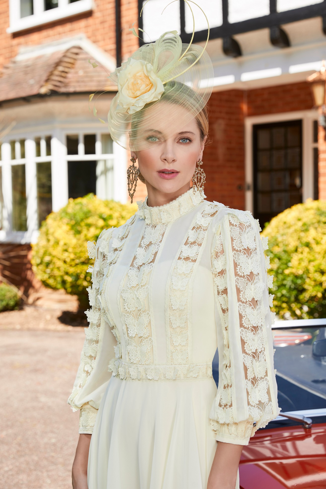 Close up image of woman wearing special occasion mother of the bride dress lemon yellow with high neckline , long sleeves and 3d butterfly detail standing in front of a house