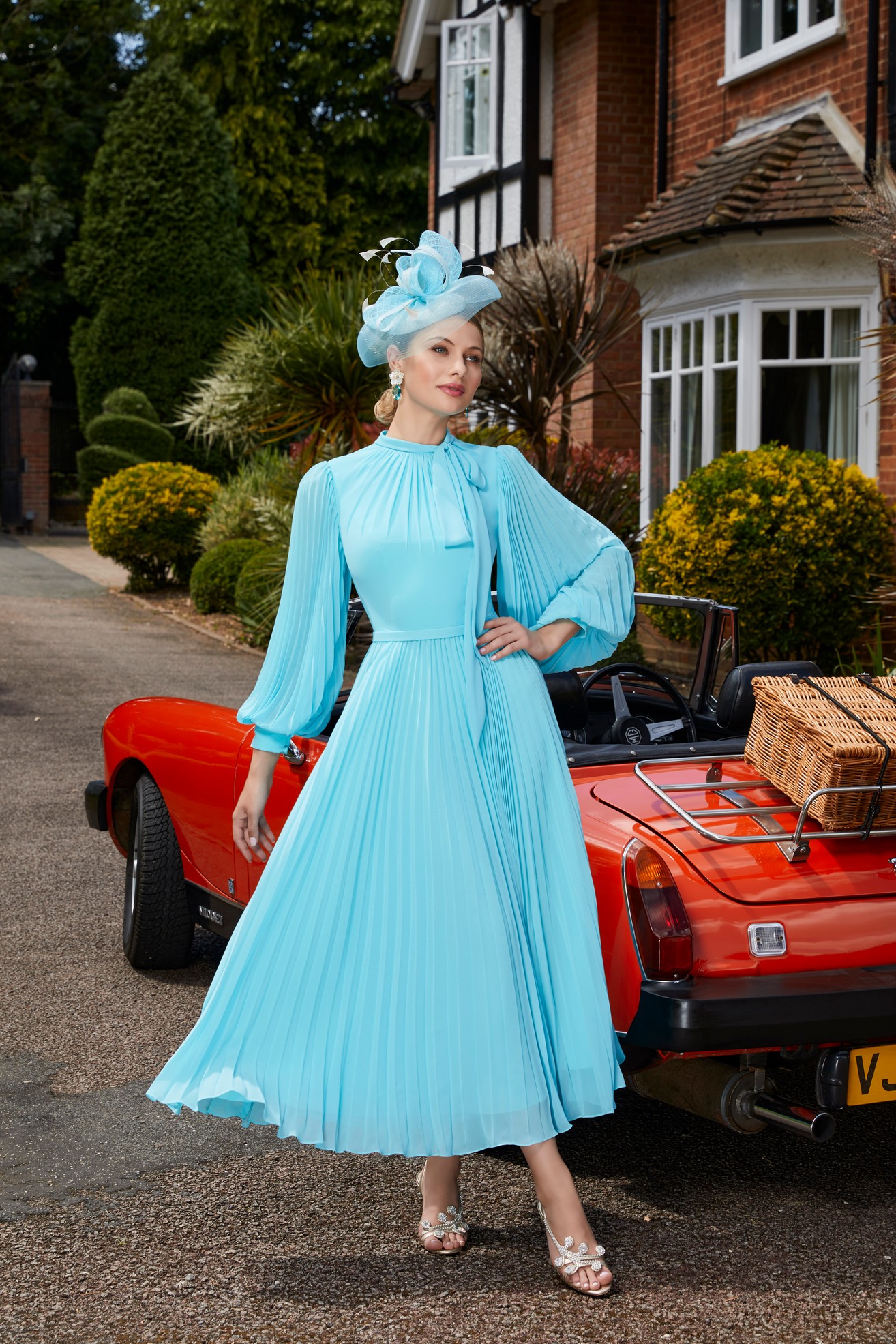 Woman standing next to vintage red car wearing vivid blue a-line dress with blouson sleeves and bow neckline detail 